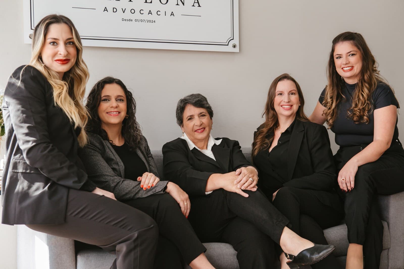 Equipe da Pamplona Advocacia reunida no sofá da recepção do escritório, sob o letreiro institucional.